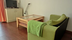 En stue med en grøn sofa, et træ sofabord, et fjernsyn på et skab og en gulvlampe.