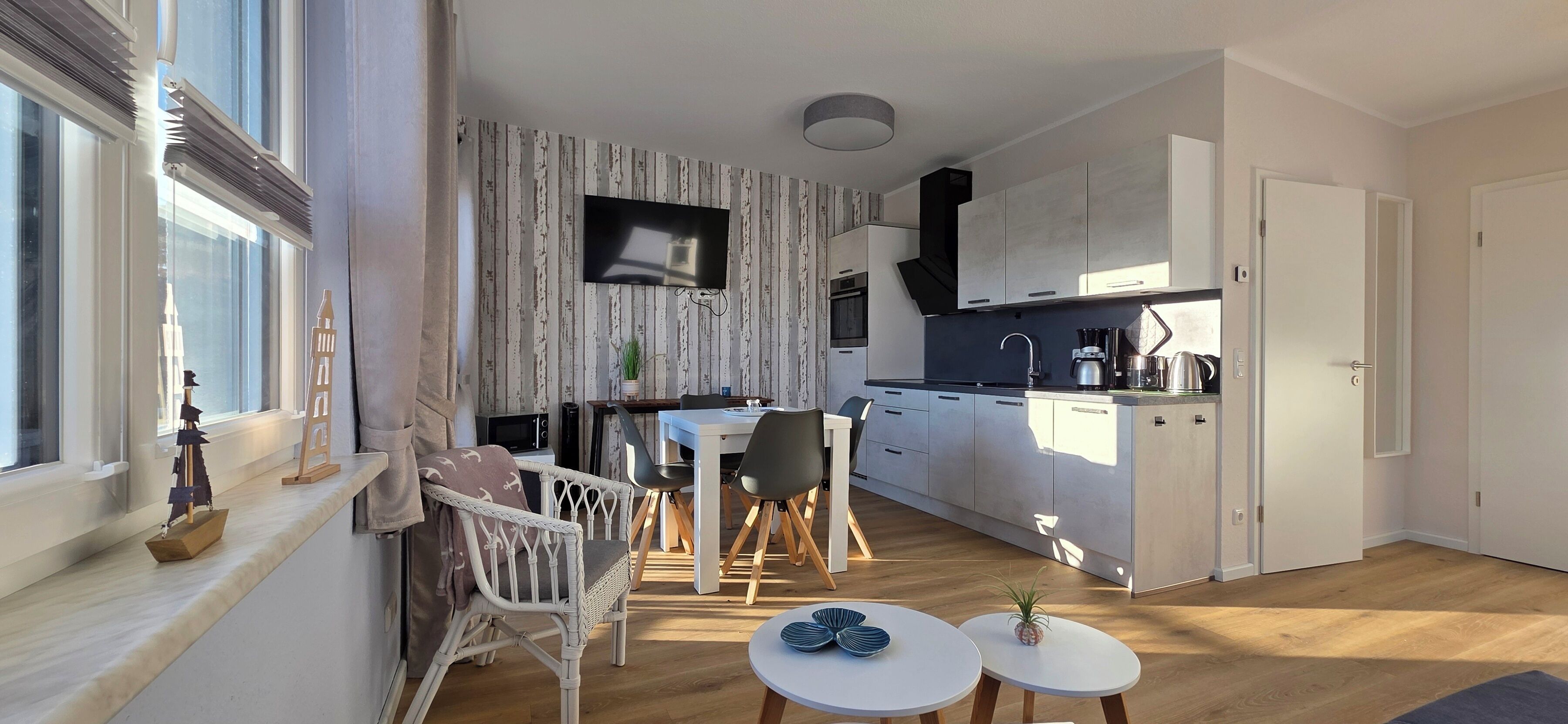 A modern kitchen with white cabinets, a black countertop, and a built-in oven. There is a dining area with a white table and chairs, and a small round table with decorative items.
