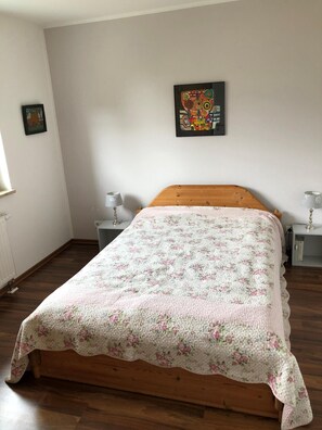 A bedroom with a wooden bed, floral bedding, two bedside tables with lamps, and a colorful abstract painting on the wall.
