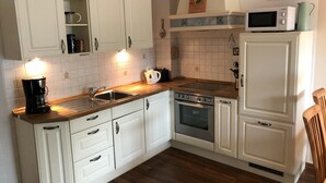 A kitchen with white cabinets, a wooden countertop, a stove, a microwave, and a sink. - 2-zi.-fewo für 4 Personen im 1. OG Links (Graal-Müritz)