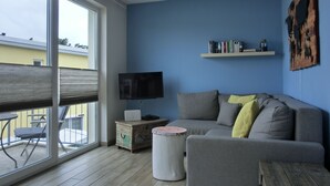 A living room with a grey sofa, a small round table, a television on a wooden stand, and a bookshelf against a blue wall. - 2-zimmer-fewo für 4 Pers. mit Wlan (Graal-Müritz)