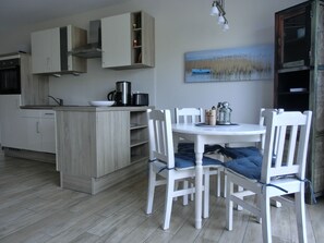 A modern kitchen with white cabinets, a dining table with white chairs, and a painting of a lake on the wall.