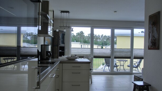 A modern kitchen with a large window, a dining area with a table and chairs, and a small stool. - 2-zimmer-fewo für 4 Pers. mit Wlan (Graal-Müritz)