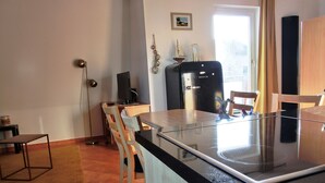 Una cocina moderna con encimera negra, sillas de madera, un refrigerador y un ventanal con cortinas.