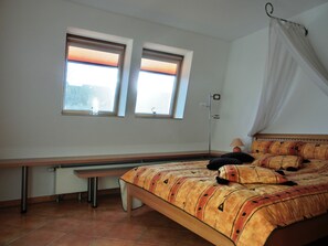 A bedroom with a bed, a desk, two windows, and a bedside lamp.