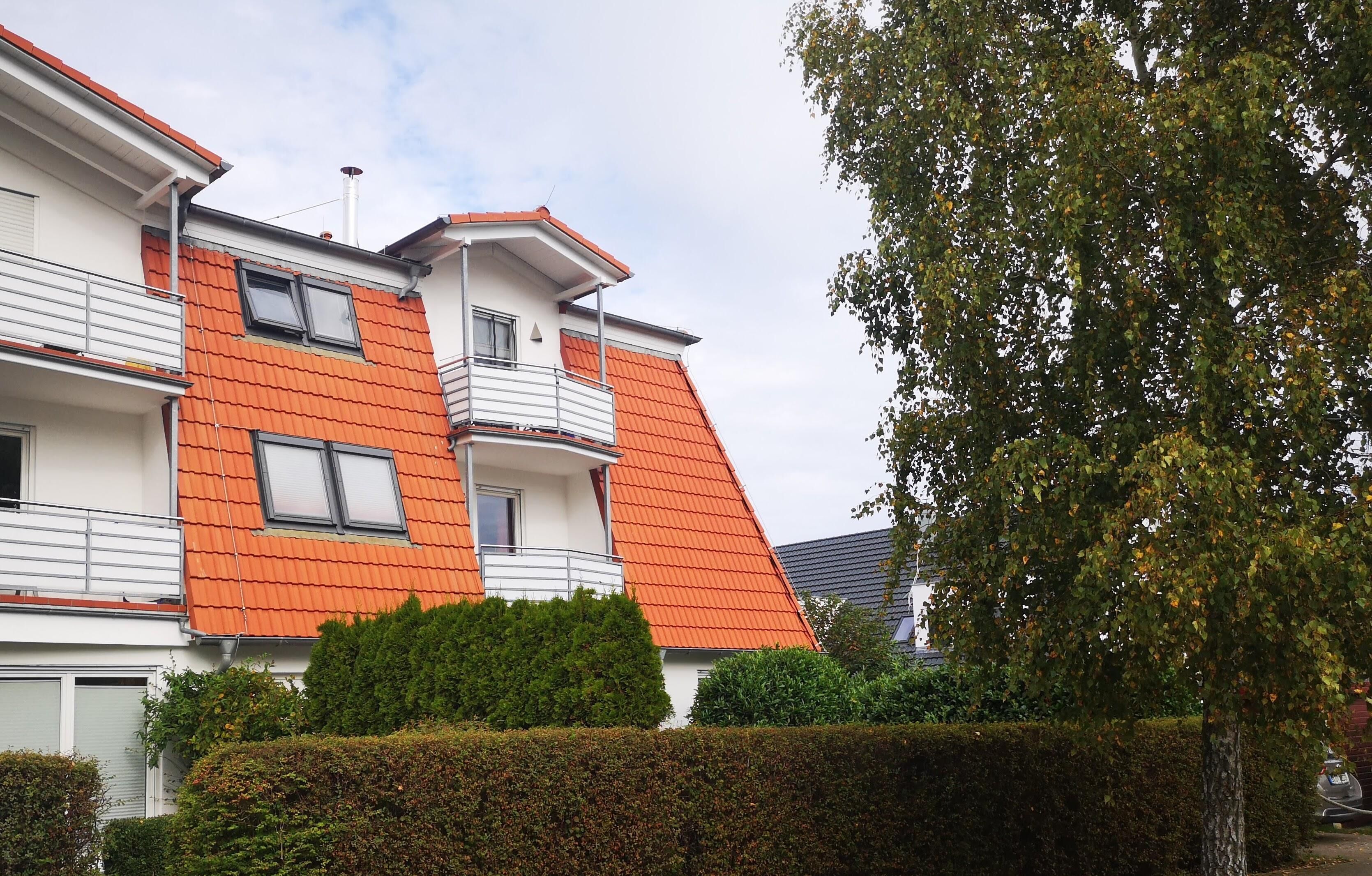 Ein mehrstöckiges Wohngebäude mit orangefarbenen Ziegeldächern, Balkonen und einer gepflegten Hecke.