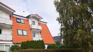 Un edificio residencial de varios pisos con tejados de tejas anaranjadas, balcones y una siega bien cuidada.