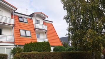 Ein mehrstöckiges Wohngebäude mit orangefarbenen Ziegeldächern, Balkonen und einer gepflegten Hecke.