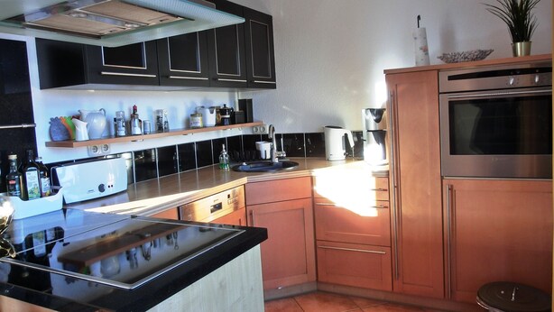 Una cocina moderna con armarios negros, una campana extractora de acero inoxidable, un horno empotrado y una cafetera.