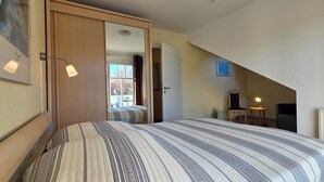 Une chambre à coucher avec un lit, une porte donnant sur une autre pièce, une petite table avec une lampe et un radiateur.