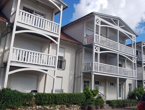 Un edificio residencial de varios pisos con balcones, un muro de piedra y un coche rojo estacionado adelante.