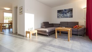 Een moderne woonkamer met een hoekbank, een houten salontafel, en een eethoek met een tafel en stoelen.