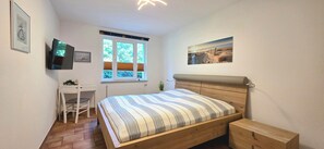 A bedroom with a bed, a desk, a chair, a window with blinds, and a painting on the wall.
