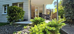A house with a covered porch, a patio with a table and chairs, and a garden with various shrubs.