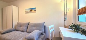 Een kamer met een bed, een stoel, een bureau, een plant en een raam.