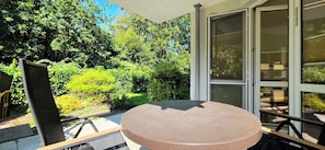 A patio with a round table and chairs, surrounded by a garden with various plants and trees.