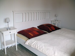Une chambre à coucher avec un lit blanc, deux oreillers, une table de chevet avec une lampe et une commode avec une lampe.