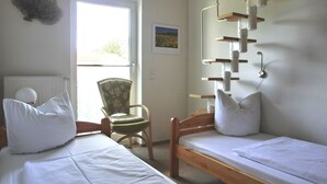 Een slaapkamer met twee eenpersoonsbedden, een stoel, een radiator en een raam.