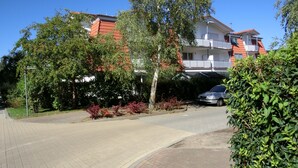 Een woonstraat met een verhard voetpad, een geparkeerde auto en een gebouw met een rood dak en balkons.