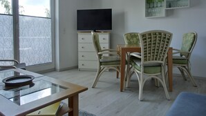 Een kamer met een eettafel, stoelen, een televisie en een glazen kast met decoratieve objecten.