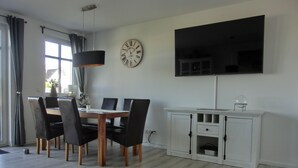 Un comedor con una mesa y sillas de madera, un reloj en la pared, un televisor de pantalla plana y un armario blanco.