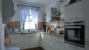 Una cocina moderna con armarios blancos, horno empotrado y ventana con cortinas.