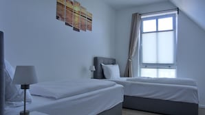 Habitación de hotel con dos camas, una mesita de noche, una lámpara, una ventana con cortinas y una obra de arte en la pared.