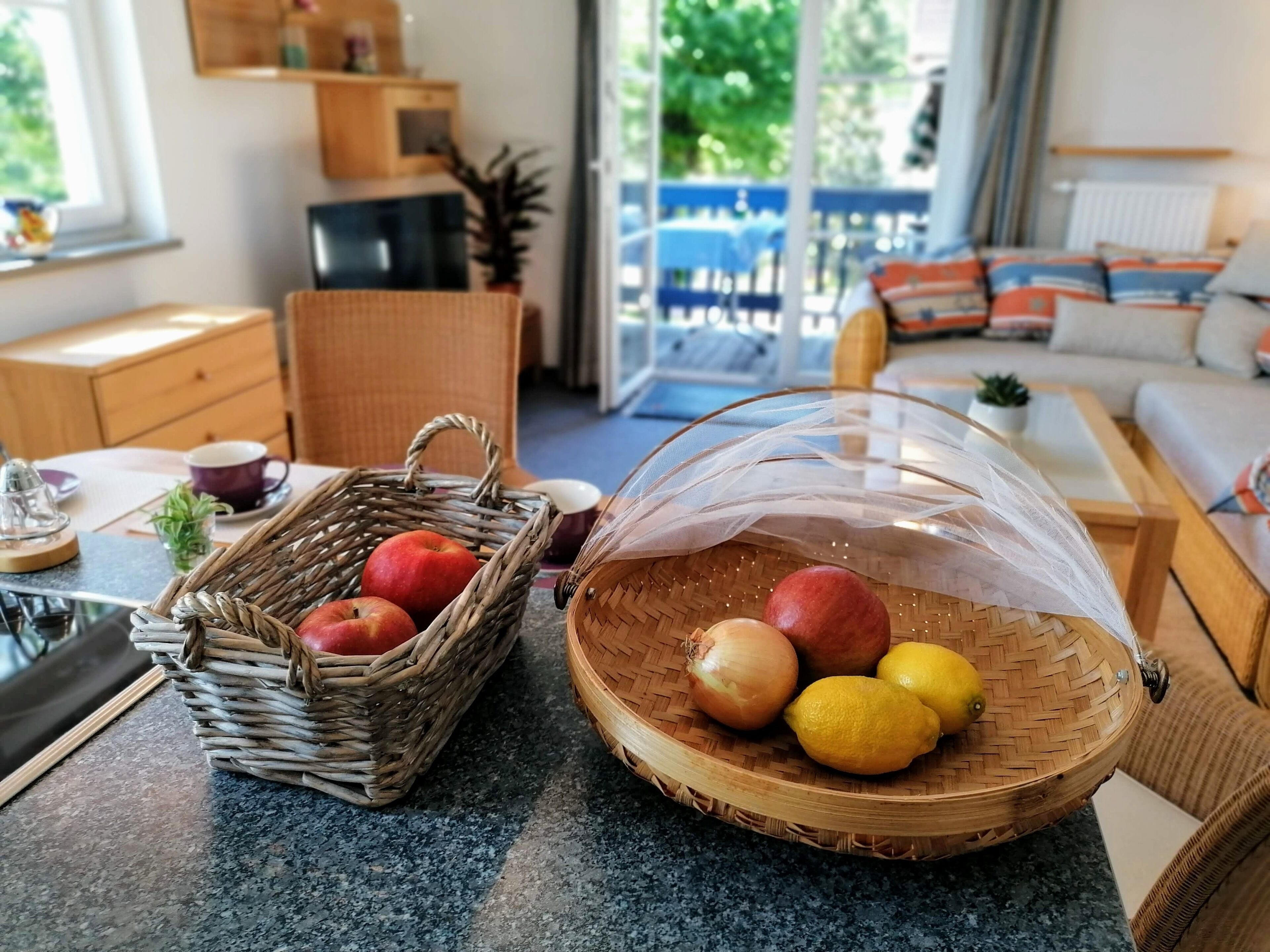 A kitchen area with wicker baskets containing apples and lemons, a coffee maker, and a wooden cabinet.