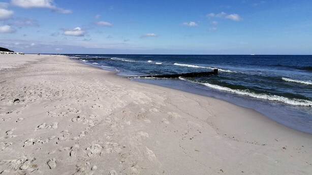 A wide sandy beach with gentle waves, a clear sky, and a distant ship. - Sonnige Wohnung mit Süd-balkon und Strandkorb - M31 (Seeheilbad Graal-Müritz)