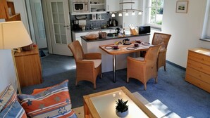A compact kitchen with white cabinets, a microwave, and a coffee maker. There is a dining table with chairs and a small potted plant. - Sonnige Wohnung mit Süd-balkon und Strandkorb - M31 (Seeheilbad Graal-Müritz)