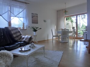 Uma sala de estar com um sofá de couro preto, uma mesa de centro branca e uma área de jantar com uma mesa e cadeiras brancas.