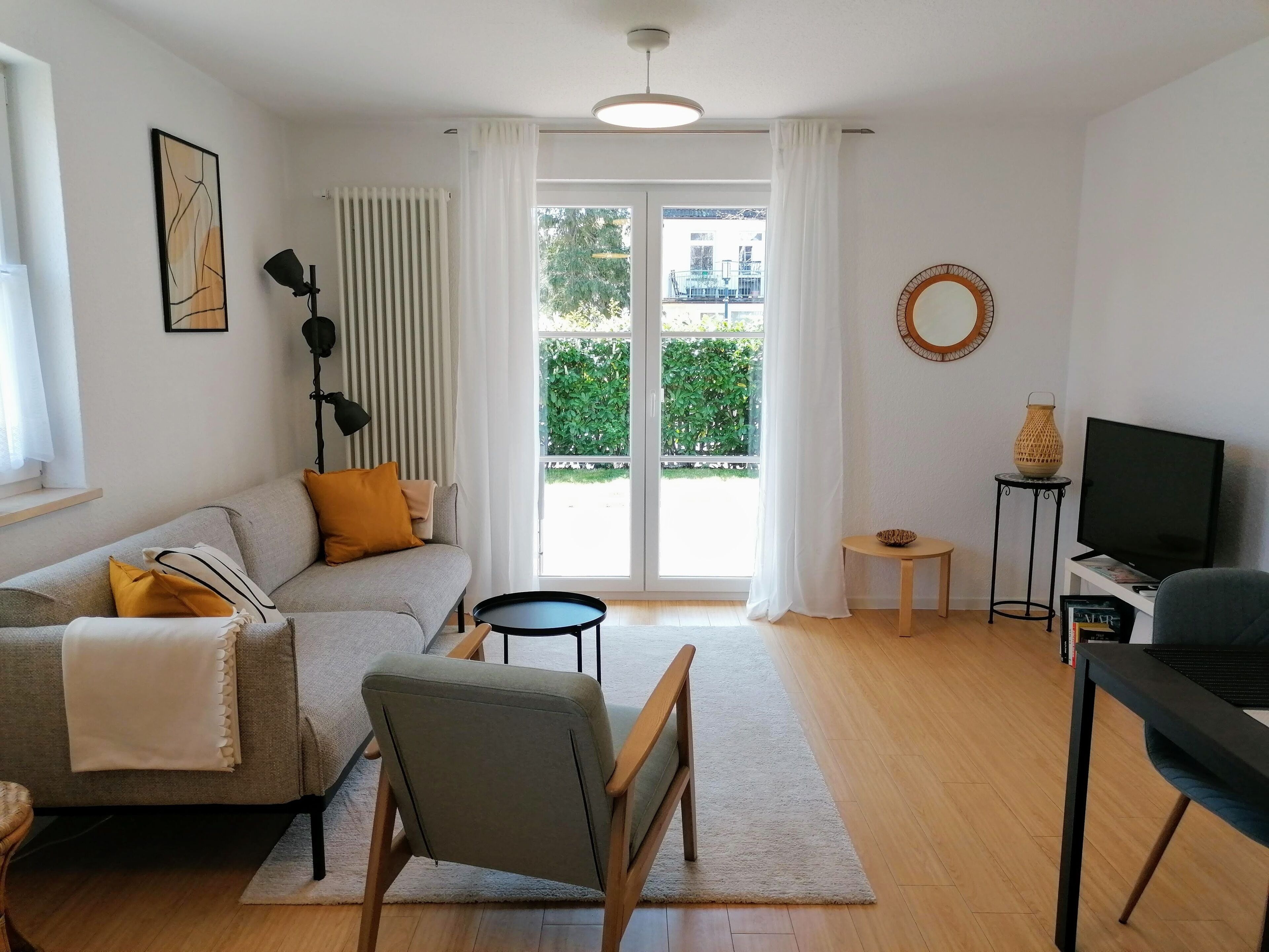 A modern living room with a sofa, a chair, a small table, a TV, and a view of greenery outside.