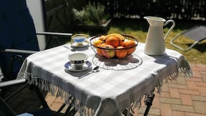 Une table recouverte d’une nappe à carreaux, un saladier rempli de fruits, une carafe, ainsi qu’une tasse et une soucoupe.