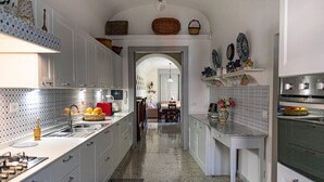 A kitchen with white cabinets, a granite countertop, and a gas stove. There is a dining area with a table and chairs visible through an archway. - BAGLIO OF SANTA MARINA (Milazzo)
