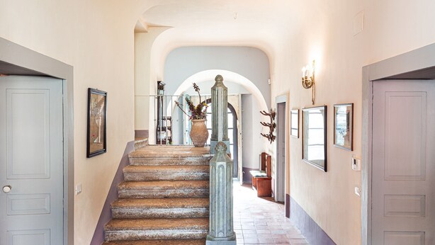 A hallway with a stone staircase, framed artwork on the walls, and a large vase with flowers. - BAGLIO OF SANTA MARINA (Milazzo)