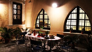 A dining area with a round table, chairs, potted plants, and a window with a grid pattern. - BAGLIO OF SANTA MARINA (Milazzo)