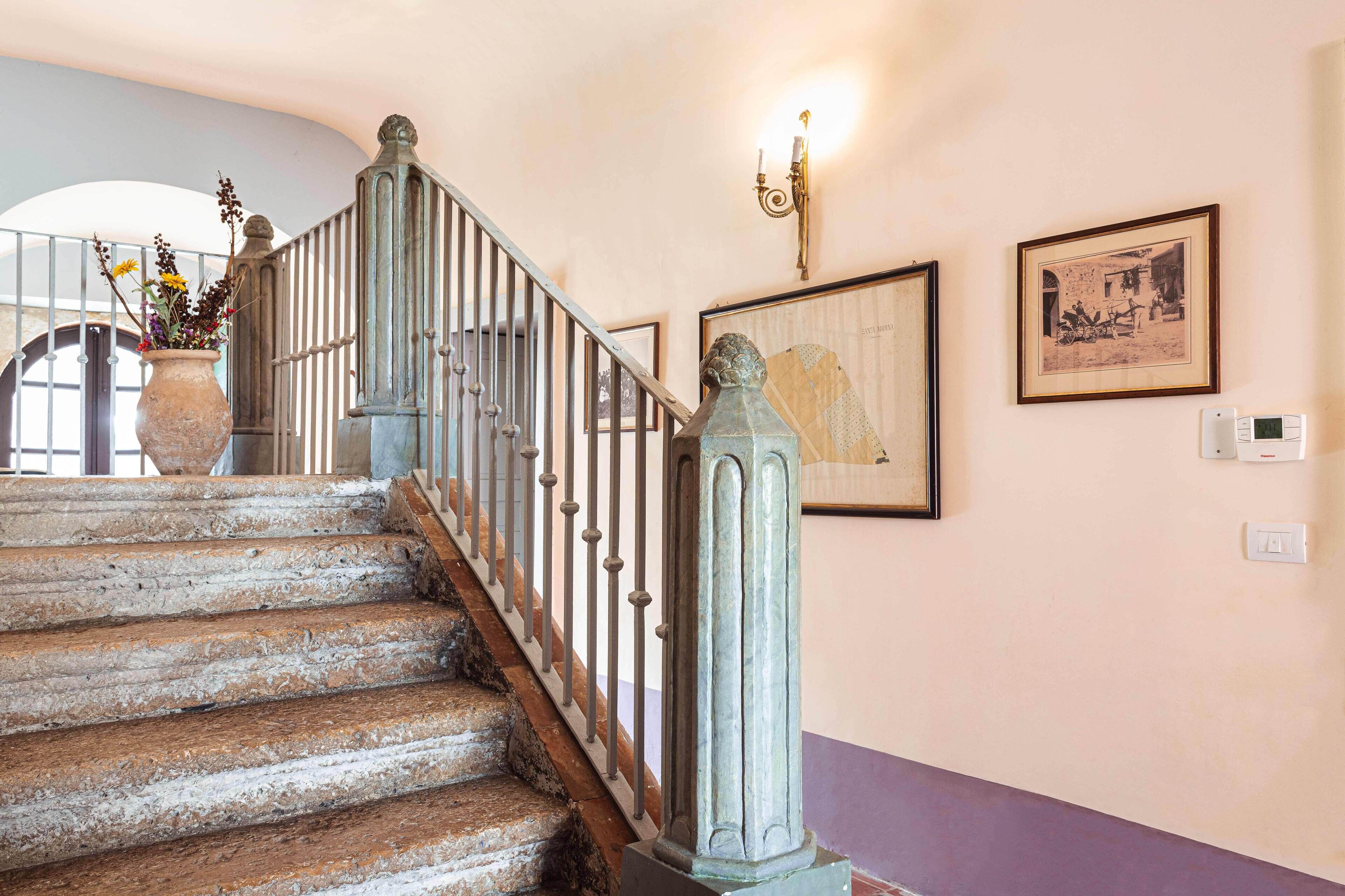 Una scala con ringhiera in ferro battuto, un vaso con fiori e quadri appesi al muro.