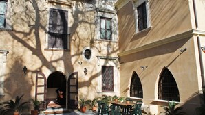 A courtyard with a table and chairs, potted plants, and a building with arched windows and a door. - BAGLIO OF SANTA MARINA (Milazzo)