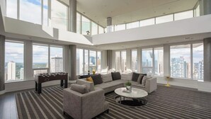 A spacious living area with a sectional sofa, a foosball table, and a round coffee table. Large windows offer a city view. - Stylish Corner Unit. Views & Comfort. Feel at Home (Calgary)