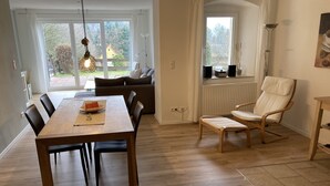 A dining area with a wooden table and chairs, a sofa, and a rocking chair. There is a large window with a view of the outdoors. - Holiday apartment Gohrisch, Landhaus Böhmer***** (Papstdorf)