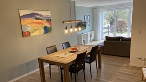 A modern dining area with a wooden table and chairs, a hanging light fixture, and a large window with a view of the outdoors. - Holiday apartment Gohrisch, Landhaus Böhmer***** (Papstdorf)