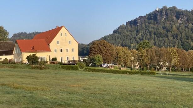 A large, two-story building with a red roof, surrounded by a grassy field and trees. - Holiday apartment Gohrisch, Landhaus Böhmer***** (Papstdorf)