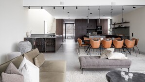 Una cocina moderna con comedor, que cuenta con una isla central, iluminación colgante y vista al salón.
