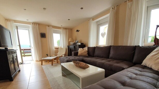 A living room with a brown leather sofa, a white coffee table, and a television on a cabinet. There is a window with curtains and a view of the outdoors. - FeWo Zirkelstein, Landhaus Böhmer***** (Papstdorf)