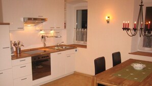 A modern kitchen with white cabinets, a wooden countertop, a built-in oven, and a dining area with a table and chairs. - FeWo Zirkelstein, Landhaus Böhmer***** (Papstdorf)