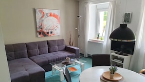 A living room with a grey sofa, a glass coffee table, a round table with a vase, and a TV on a stand. - Apartment Papststein, Landhaus Böhmer***** (Papstdorf)