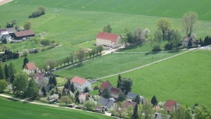 Eine ländliche Landschaft mit einem großen weißen Gebäude, umgeben von kleineren Häusern, Feldern und einer Straße.