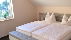 Ein Schlafzimmer mit zwei Betten, einem Fenster mit Pflanze und einer schrägen Decke.