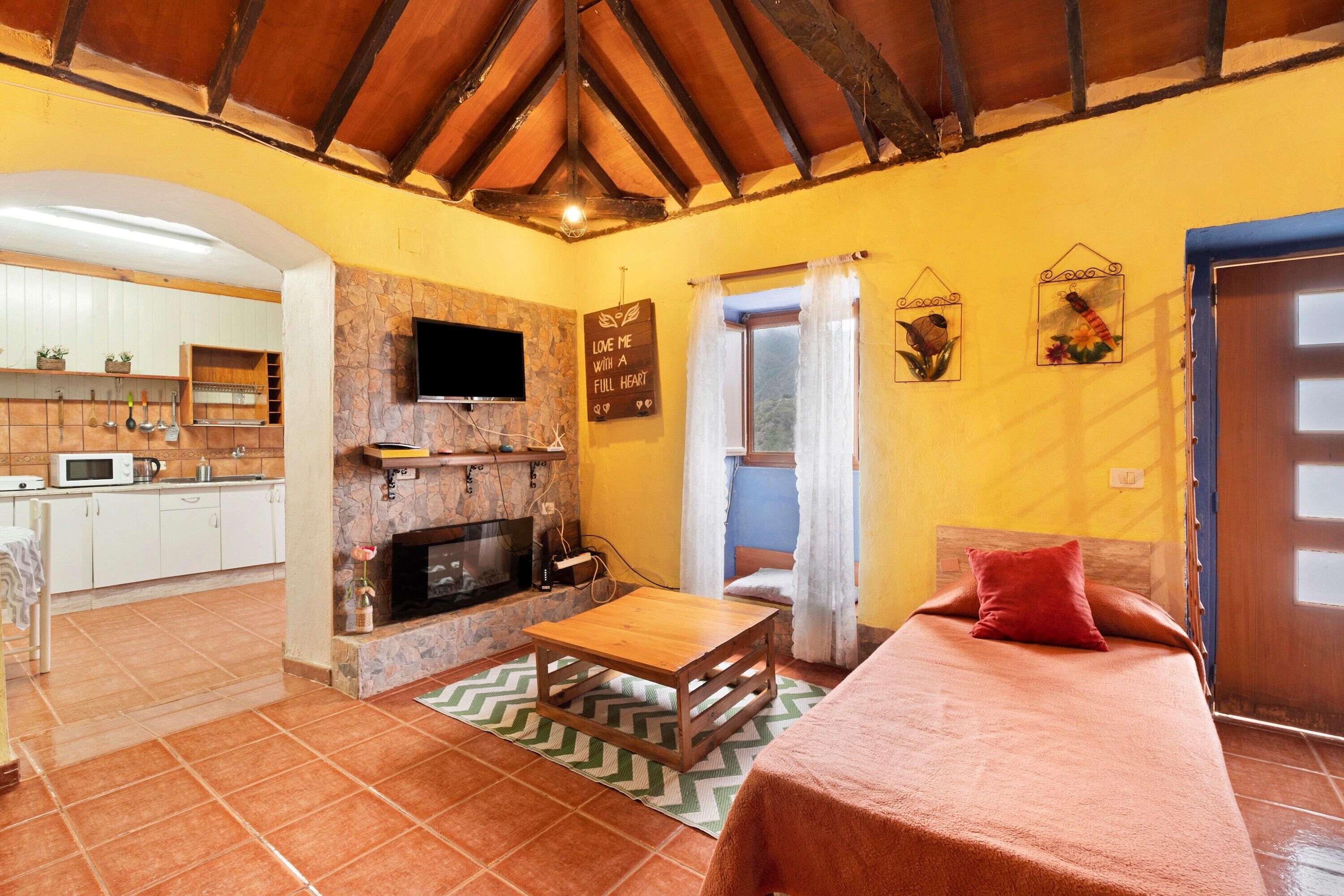 Una habitación acogedora con una cama, una mesa de madera, una chimenea, una zona de cocina y un televisor.