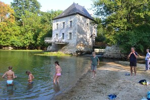 A stone building with a balcony overlooking a body of water, surrounded by trees. - Mill with terrace on the water - variety, charm & space. (Monts)